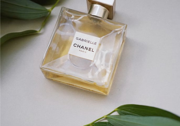 CHANEL's Gabrielle Perfume on a white table surrounded by green leaves