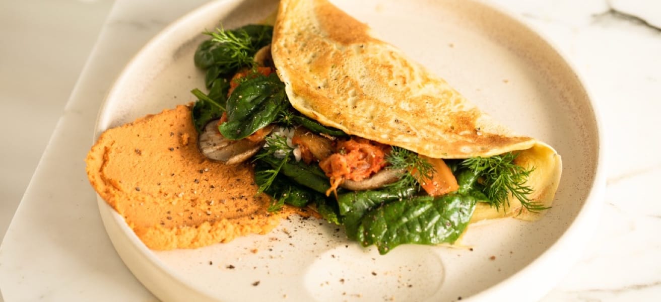 Delicious omelette stuffed with spinach and diced vegetables with herbs on a white plate